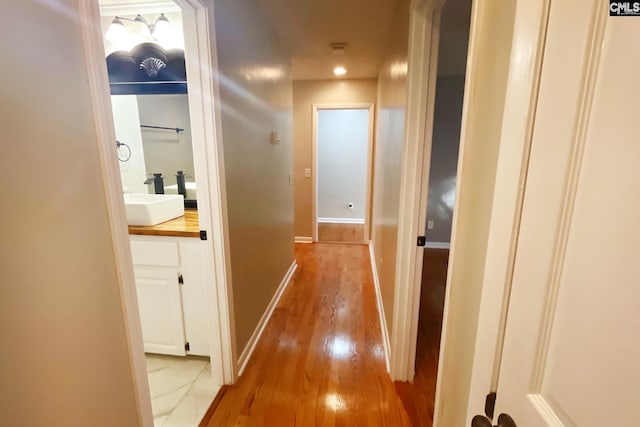 corridor featuring light wood-style flooring, baseboards, and a sink