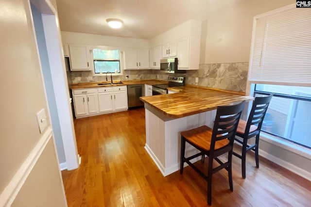 kitchen with butcher block countertops, a peninsula, stainless steel appliances, white cabinetry, and a sink