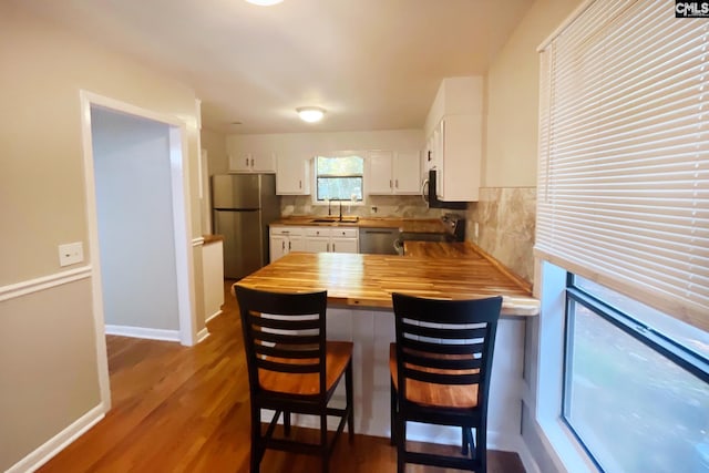 kitchen featuring butcher block countertops, a sink, white cabinetry, stainless steel appliances, and a peninsula