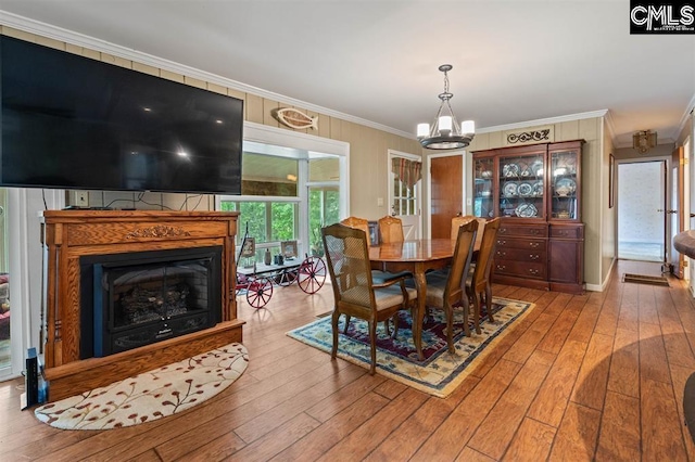 dining area featuring wood-type flooring, an inviting chandelier, a glass covered fireplace, and crown molding