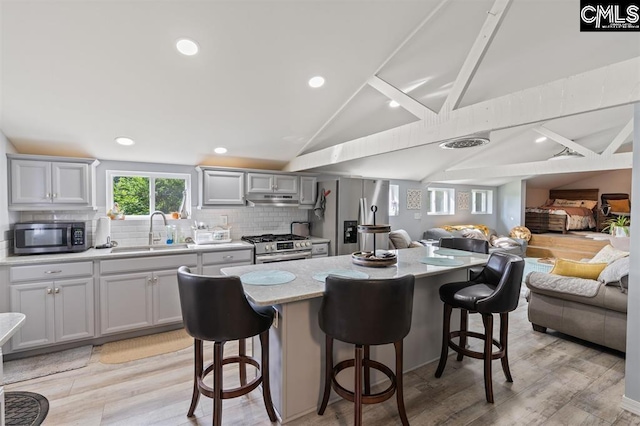 kitchen featuring a sink, under cabinet range hood, open floor plan, stainless steel appliances, and lofted ceiling