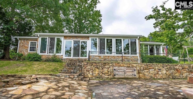 rear view of property with fence, a lawn, a sunroom, stone siding, and a patio