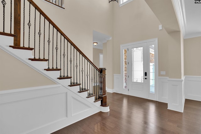 entrance foyer featuring stairs, dark wood-type flooring, a decorative wall, and wainscoting