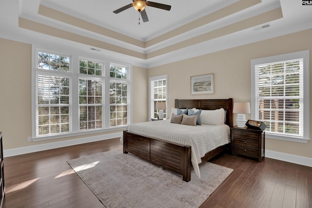 bedroom with baseboards, crown molding, a tray ceiling, and dark wood-style flooring