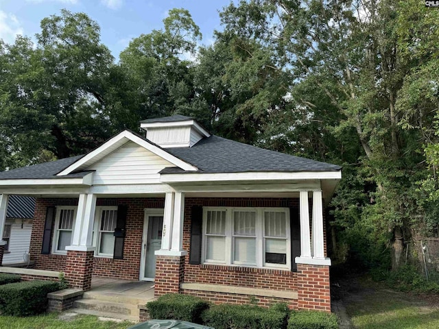 bungalow-style house with covered porch, brick siding, and a shingled roof