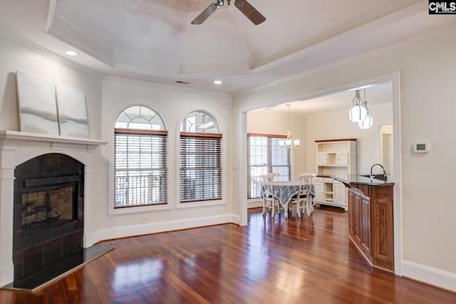 living room with a fireplace with raised hearth, crown molding, baseboards, dark wood finished floors, and a raised ceiling