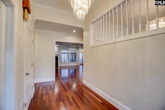 hall featuring a notable chandelier, baseboards, wood-type flooring, and ornamental molding