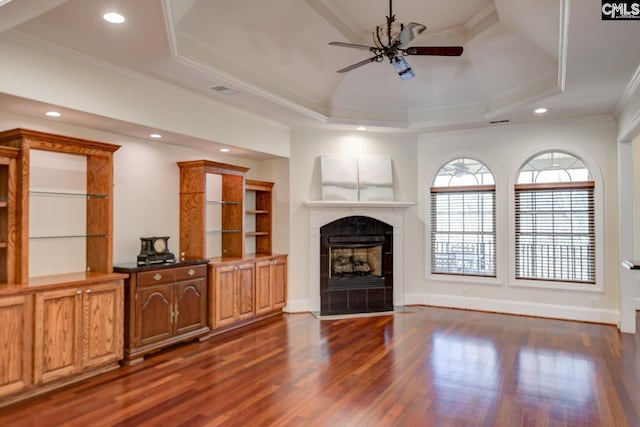 living area with a tray ceiling, dark wood-style floors, a fireplace, crown molding, and ceiling fan