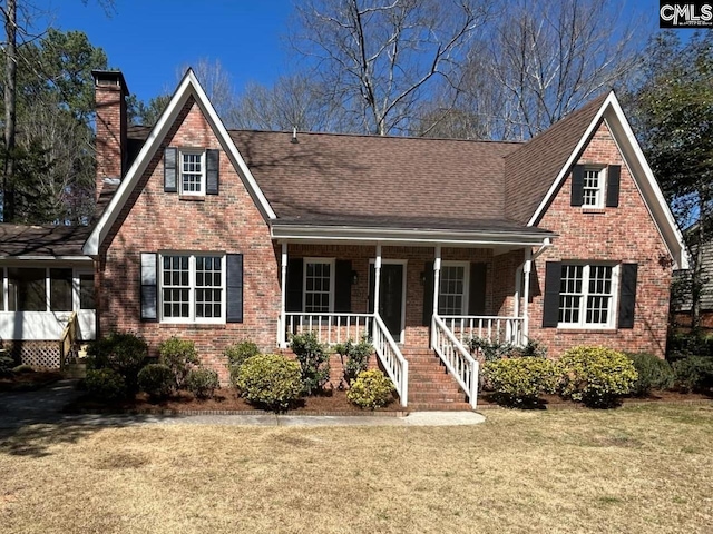 tudor-style house featuring brick siding, a porch, a chimney, and a front yard