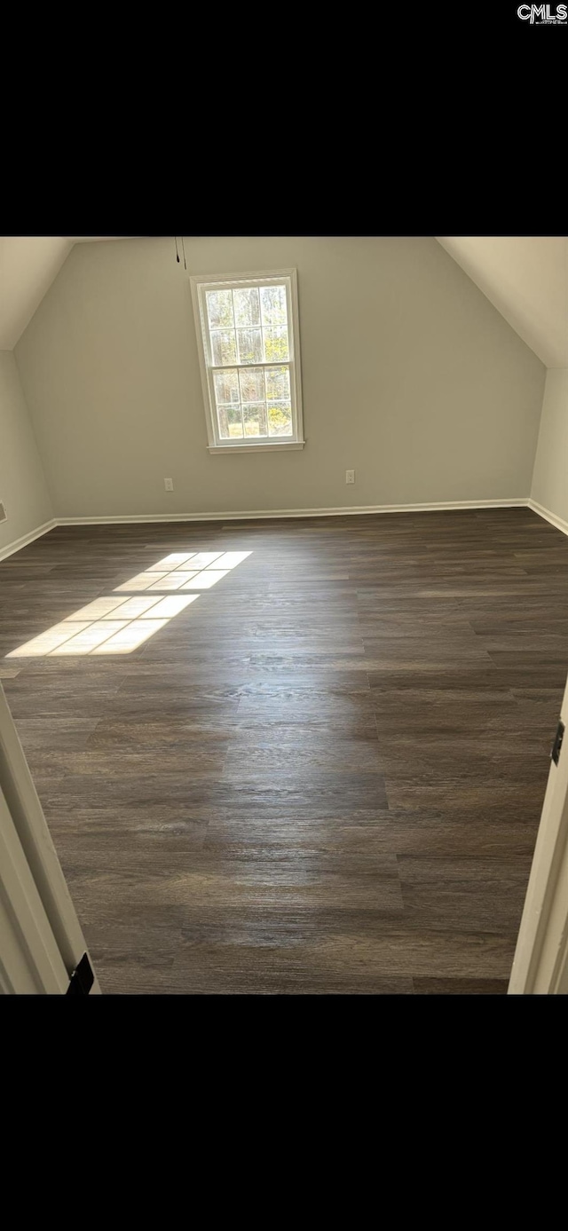 additional living space featuring baseboards, dark wood-style floors, and vaulted ceiling