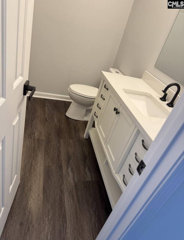 half bathroom with toilet, vanity, baseboards, and wood finished floors