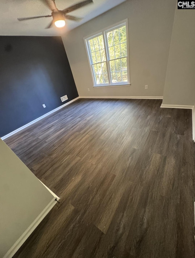 unfurnished room featuring baseboards, visible vents, dark wood-style flooring, and ceiling fan