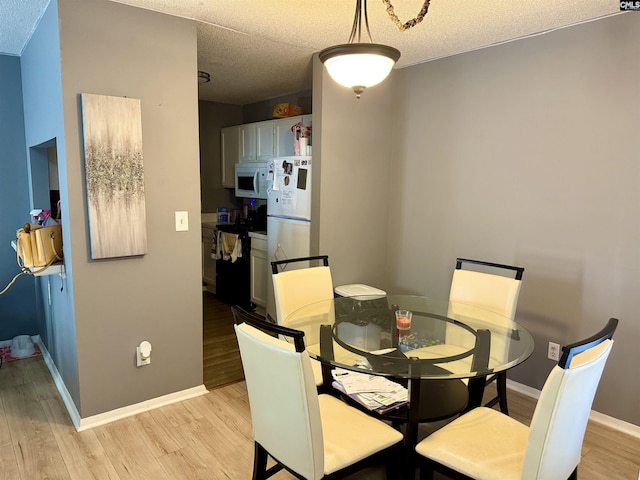 dining area featuring light wood-style floors, baseboards, and a textured ceiling