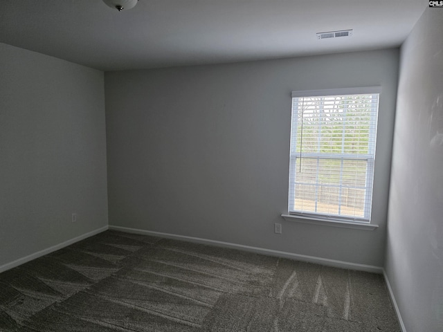 spare room featuring visible vents, baseboards, and dark carpet