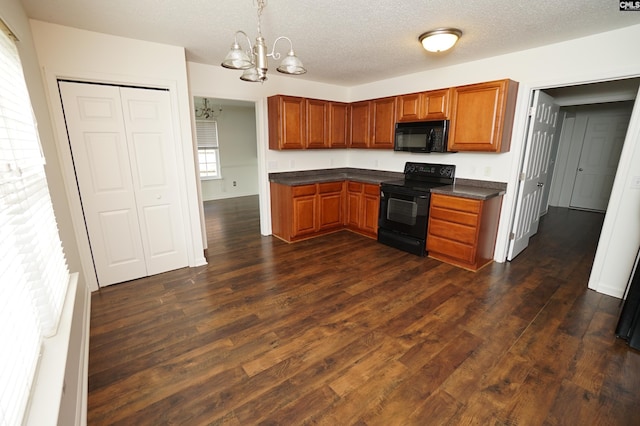 kitchen featuring dark countertops, black appliances, dark wood finished floors, and an inviting chandelier