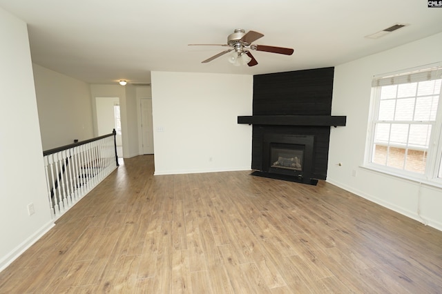 unfurnished living room featuring a ceiling fan, visible vents, light wood finished floors, baseboards, and a fireplace