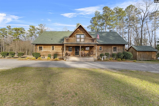 cabin featuring a front yard, a balcony, an outbuilding, driveway, and a storage unit