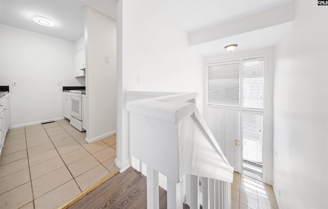 hall featuring light tile patterned flooring, a healthy amount of sunlight, and baseboards