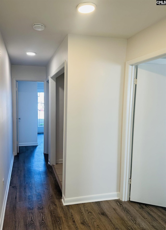 corridor featuring dark wood-type flooring and baseboards