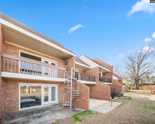 back of property featuring brick siding, a balcony, stairs, and a patio area