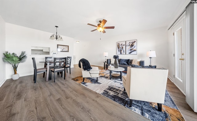 living room featuring ceiling fan with notable chandelier, wood finished floors, and baseboards