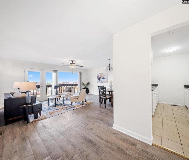 living room featuring light wood-style flooring, ceiling fan with notable chandelier, and baseboards