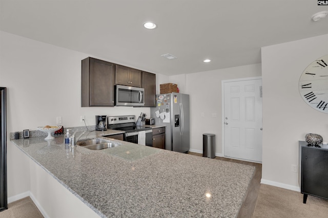 kitchen featuring light stone countertops, a peninsula, a sink, dark brown cabinetry, and appliances with stainless steel finishes