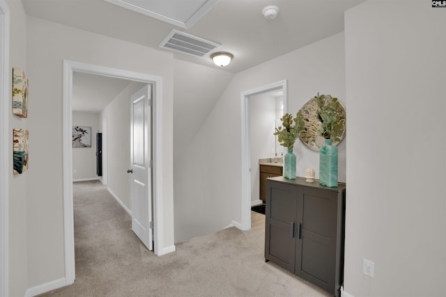 hallway with an upstairs landing, visible vents, light colored carpet, and baseboards