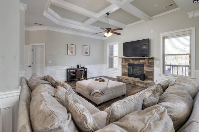 living area with visible vents, beam ceiling, a stone fireplace, wainscoting, and coffered ceiling