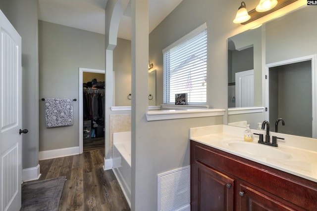 full bathroom featuring visible vents, a walk in closet, wood finished floors, a bath, and vanity