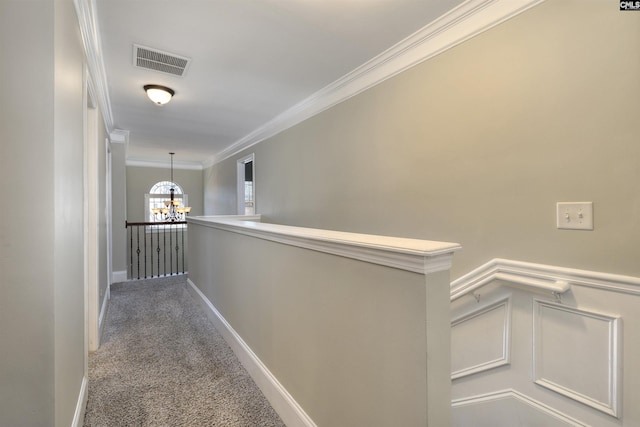 hall featuring carpet, visible vents, crown molding, a decorative wall, and a notable chandelier