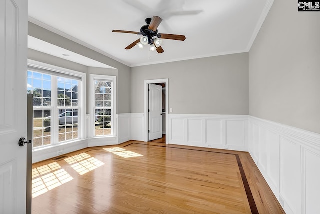 empty room with a ceiling fan, crown molding, light wood-style floors, and wainscoting