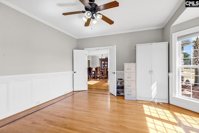 unfurnished bedroom with light wood-type flooring, ceiling fan with notable chandelier, a closet, wainscoting, and crown molding