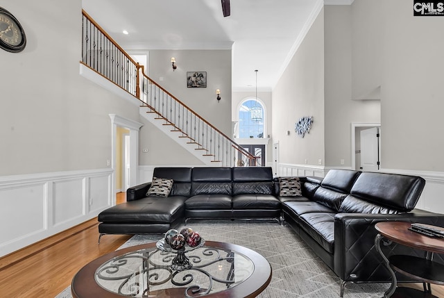 living room with crown molding, stairway, wood finished floors, and a wainscoted wall