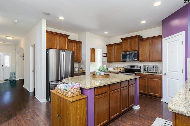 kitchen with stainless steel appliances, arched walkways, dark wood finished floors, and decorative backsplash