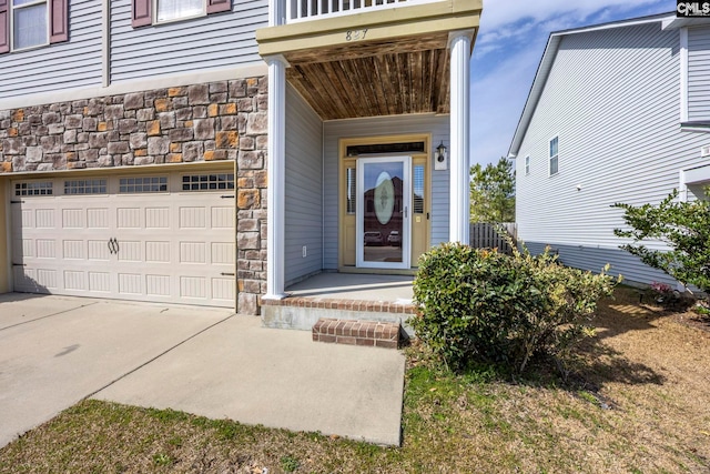 entrance to property featuring a garage, stone siding, and driveway