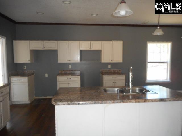 kitchen featuring a center island with sink, a sink, dark wood-style floors, white cabinets, and crown molding