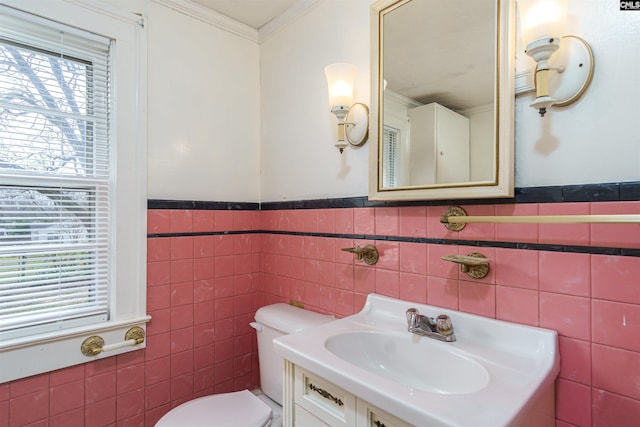 half bathroom featuring a wainscoted wall, toilet, ornamental molding, tile walls, and vanity