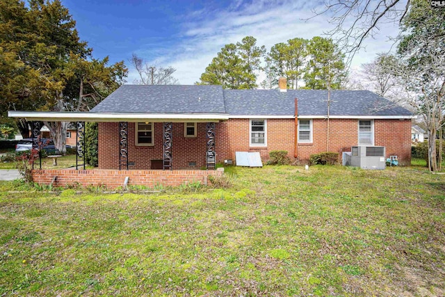 back of house with central AC, a yard, a shingled roof, brick siding, and a chimney