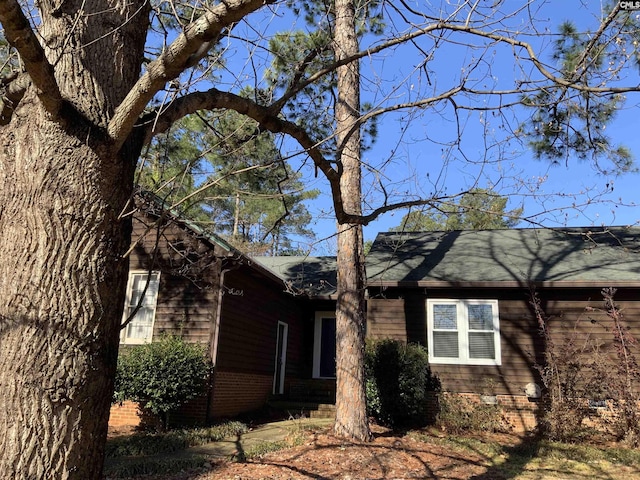 view of side of property featuring brick siding and roof with shingles