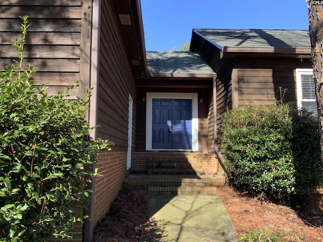 view of exterior entry with roof with shingles