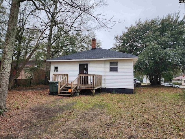 back of property with a wooden deck, a chimney, and a shingled roof