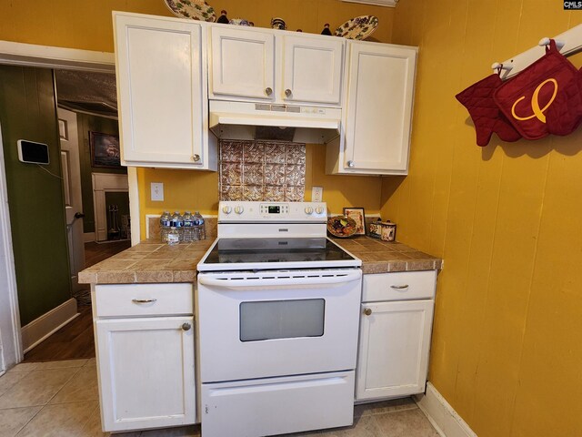 kitchen with white range with electric cooktop, under cabinet range hood, white cabinetry, wood walls, and light tile patterned floors