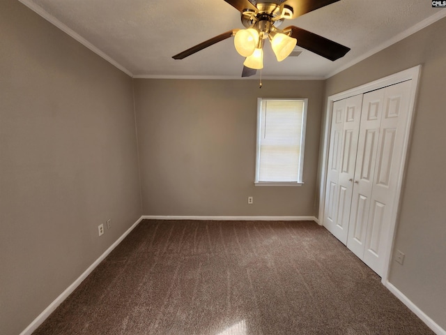 unfurnished bedroom featuring ornamental molding, a ceiling fan, dark carpet, a closet, and baseboards