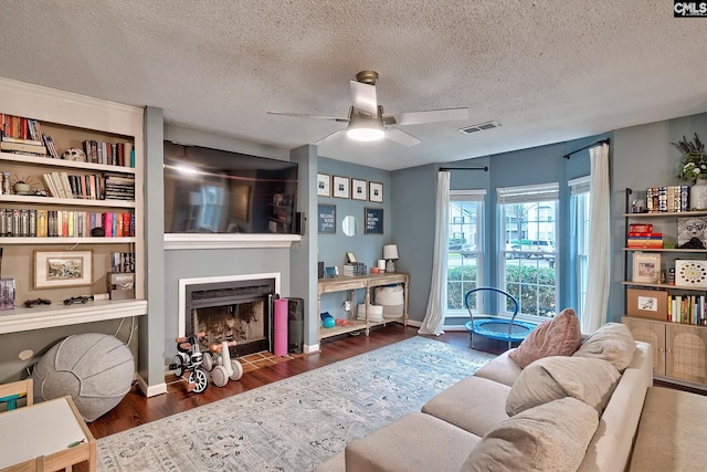 living room with a fireplace with flush hearth, wood finished floors, visible vents, and a textured ceiling