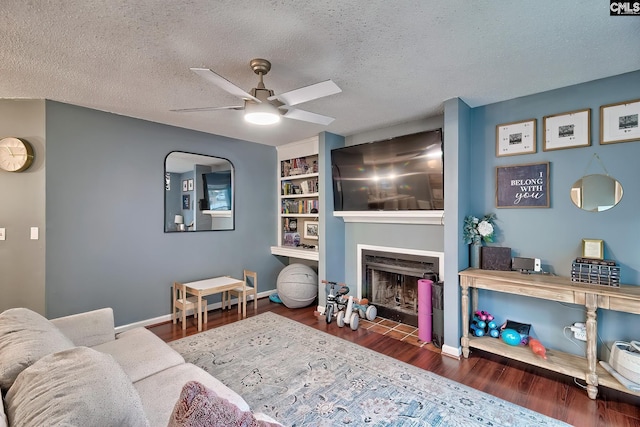 living room featuring baseboards, a fireplace with flush hearth, a textured ceiling, and wood finished floors