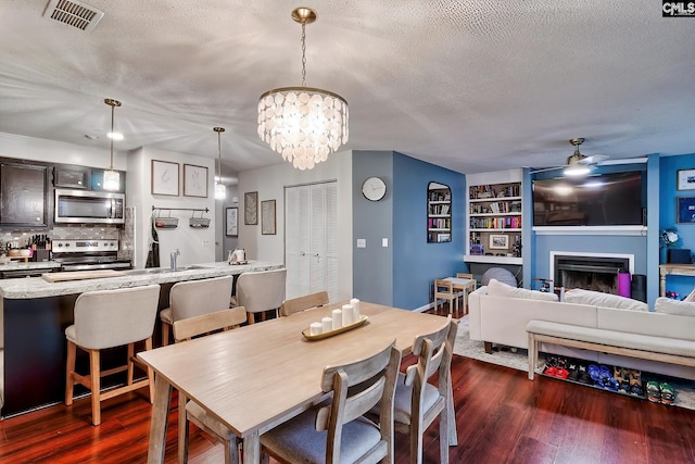 dining room with visible vents, a fireplace, dark wood-type flooring, a textured ceiling, and ceiling fan with notable chandelier