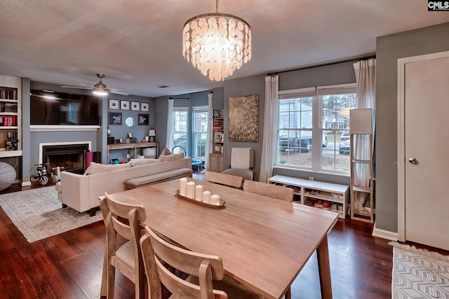 dining area featuring dark wood-style floors, ceiling fan with notable chandelier, a fireplace, and a textured ceiling