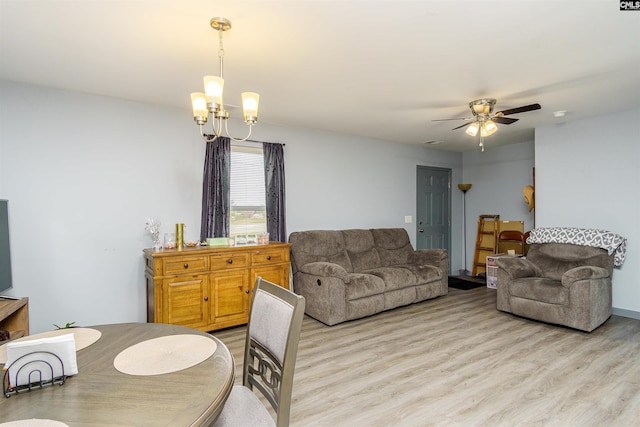 living area featuring light wood-style flooring, ceiling fan with notable chandelier, and visible vents