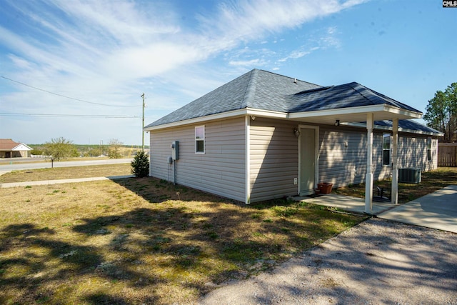 view of side of property featuring central AC unit, a lawn, roof with shingles, and a patio area